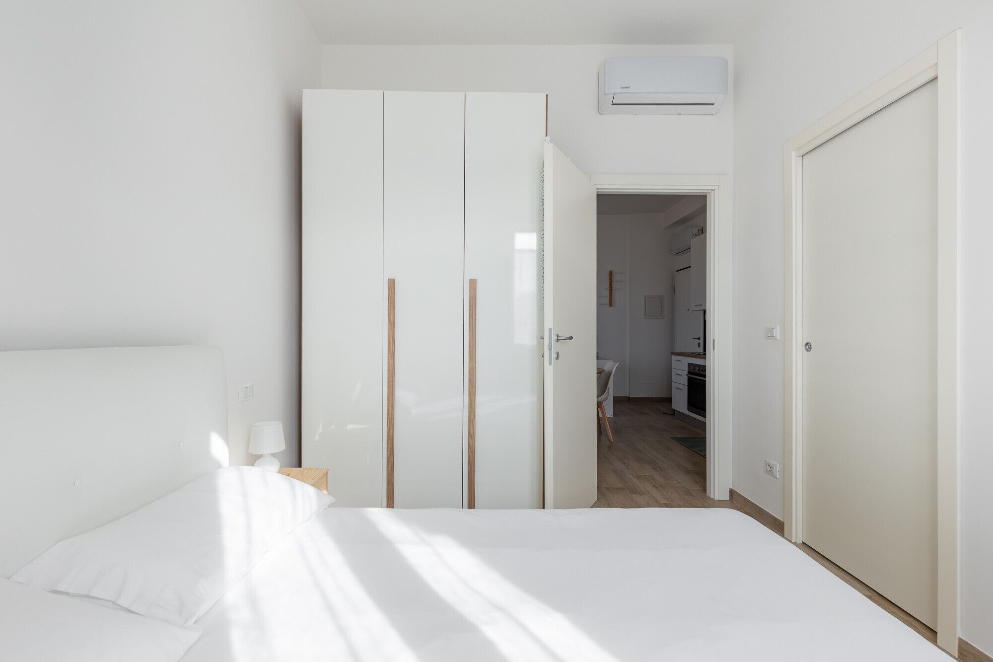A bedroom with a bed, a wardrobe, and an open door leading to a kitchen area.