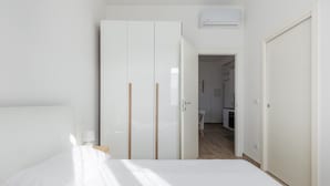 A bedroom with a bed, a wardrobe, and an open door leading to a kitchen area. - Menganti White Apartment by Wonderful Italy (Bologna)