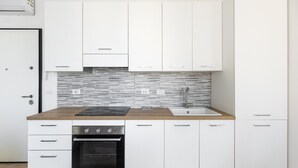 A modern kitchen with white cabinets, a stainless steel oven, a black induction cooktop, and a tiled backsplash. - Menganti White Apartment by Wonderful Italy (Bologna)
