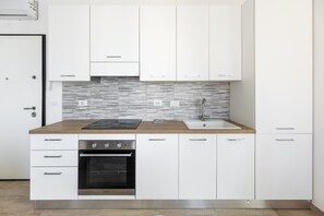 A modern kitchen with white cabinets, a stainless steel oven, a black induction cooktop, and a tiled backsplash. - Menganti White Apartment by Wonderful Italy (Bologna)