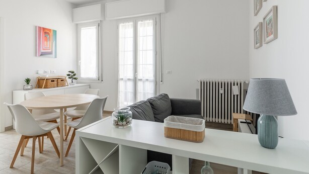 A modern, well-lit room with a dining table, chairs, a sofa, a lamp, and a radiator. - Menganti White Apartment by Wonderful Italy (Bologna)