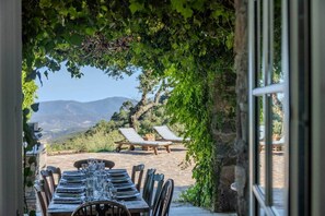 Un espace extérieur aménagé pour les repas, avec une table dressée pour quatre personnes, entourée de chaises, et une vue sur les montagnes en arrière-plan.