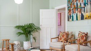 Een woonkamer met een ronde houten salontafel, een plant in pot, een witte deur en een schilderij aan de muur.