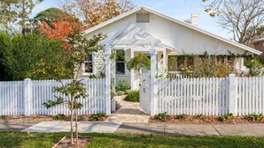 Een wit huis met een overdekte veranda, een witte picket fence en een pad dat naar de ingang leidt.