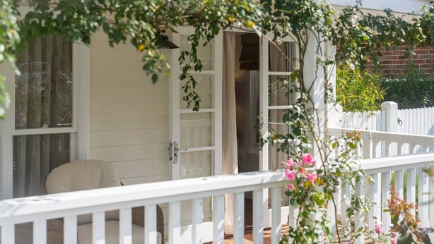 Een wit huis met een witte veranda, een witte hek en een tuin met roze bloemen.