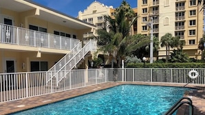 Une piscine dotée d’une balustrade blanche et d’un panneau indiquant qu’il est interdit de plonger, entourée d’un bâtiment avec des balcons et des palmiers.