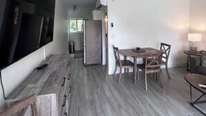 Un salon moderne doté d’un téléviseur à écran plat, d’un coin repas avec une table et des chaises, d’un ventilateur de plafond et d’un coin cuisine équipé d’un réfrigérateur.