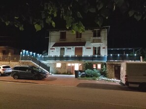 A two-story building with a balcony, a staircase, and a parking area with cars.