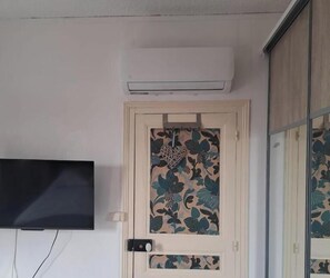 A room with a door featuring a floral pattern, a mounted air conditioner, and a television on the wall.