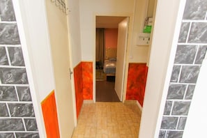 A narrow hallway with a tiled floor, leading to a room with a bed and a window.