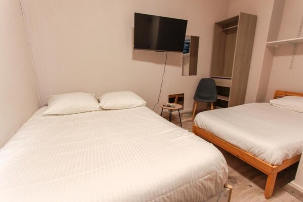 A bedroom with two beds, a TV, a chair, and a wardrobe.