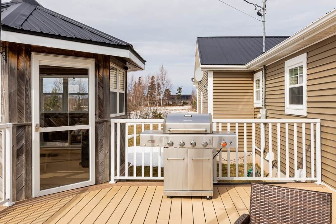 Une terrasse avec un barbecue, une porte-fenêtre coulissante et une clôture blanche.