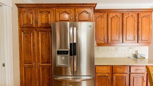 Un réfrigérateur en acier inoxydable dans une cuisine dotée de meubles en bois et d’un dosseret de carrelage blanc.