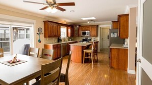 Une cuisine avec des meubles de rangement en bois, une table à manger avec des chaises, un ventilateur de plafond et un four à micro-ondes.