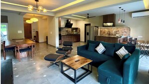 A modern living room with a sofa, coffee table, and chairs. There is a kitchen area with a microwave and cabinets. - 2 BHK/3 BED Luxury Private Pool Villa with view (Siolim)