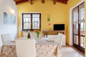 A dining area with a table set for four, a TV, and a window with curtains.