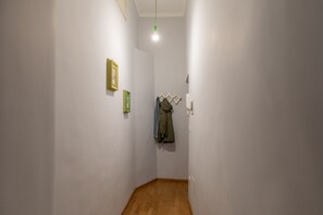 A narrow hallway with white walls, a wooden floor, and a hanging coat rack with a jacket. - iFlat | Central Rome Retreat (Rome)