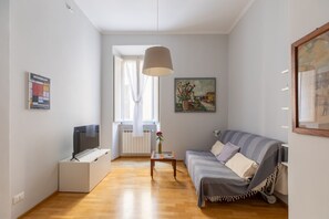 A living room with a sofa, a TV, a painting, and a window with curtains. - iFlat | Central Rome Retreat (Rome)
