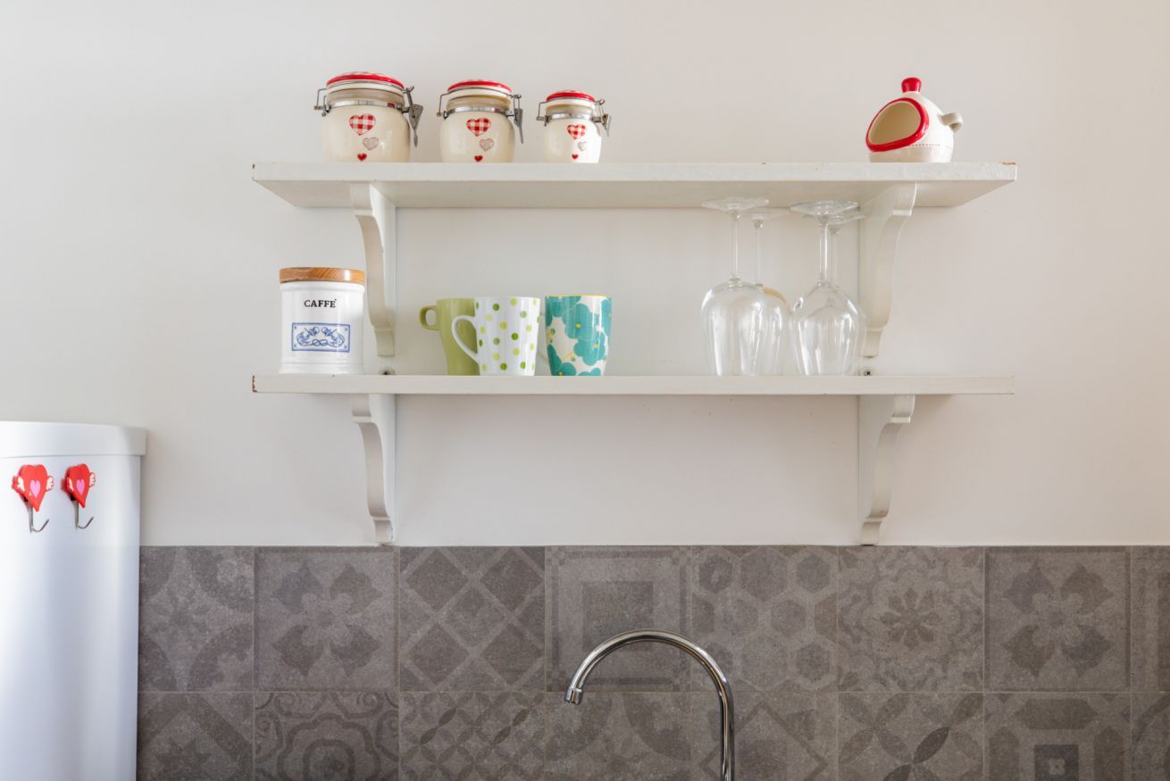 A kitchen with white shelves holding jars, a container labeled 'CAFFE,' and a glass.
