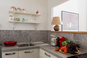 A modern kitchen with a sink, a red kettle, a toaster, and a variety of fresh vegetables on the counter. - iFlat | Central Rome Retreat (Rome)