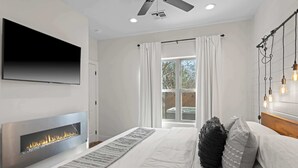 Ein modernes Schlafzimmer mit Kamin, Flachbildfernseher, Deckenventilator und großem Fenster mit Vorhängen.