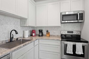 A kitchen with white cabinets, a stainless steel sink, a coffee maker, a microwave, and an oven. - Broken Windmill Cottage - Hot Tub, 5 Min to Main (Fredericksburg)