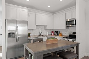 A modern kitchen with white cabinets, stainless steel appliances, a wooden table, and a built-in plant. - Broken Windmill Cottage - Hot Tub, 5 Min to Main (Fredericksburg)