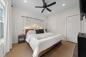 A bedroom with a bed, bedside table, ceiling fan, string lights, and a wardrobe. - Broken Windmill Cottage - Hot Tub, 5 Min to Main (Fredericksburg)