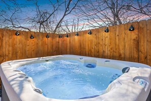 Ein Whirlpool mit Holzzaun und Beleuchtung, umgeben von Bäumen.
