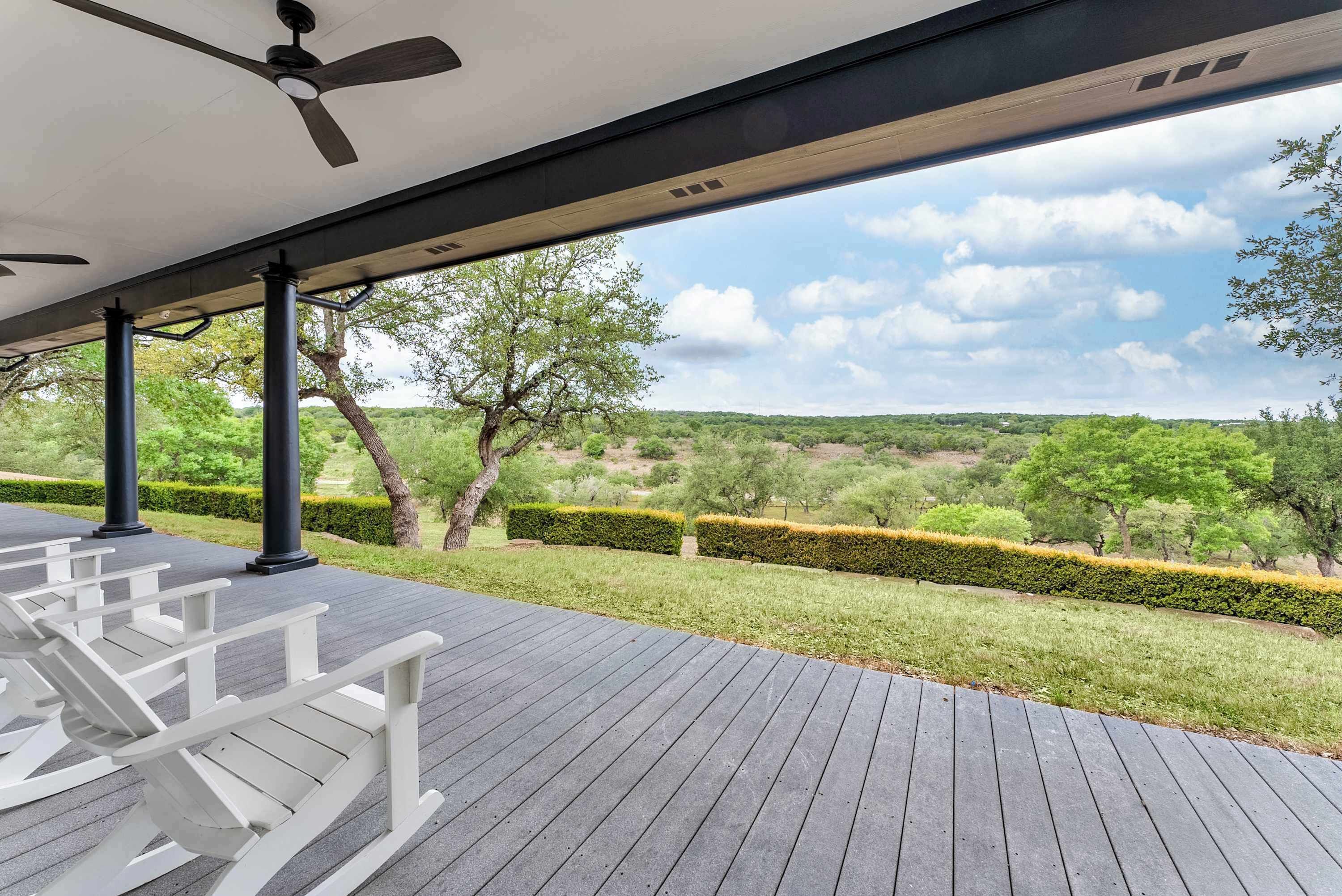 Un espace extérieur abrité offrant une vue sur un jardin aménagé et sur des collines lointaines.