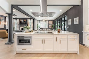 A modern kitchen with a central island, built-in oven, and stainless steel range hood. - Crown Jewel - Resort Style Pool & Sleeps 46 (Austin)