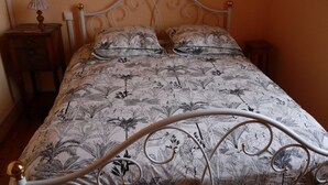 A bed with a floral-patterned bedspread, a metal headboard, and two bedside tables with lamps. - Rural Cottage at Claudette's (Briord)