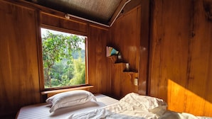 A wooden room with a bed, a window with a view of greenery, and a shelf with books. - Vietnam Village Homestay (Ha Giang 1)