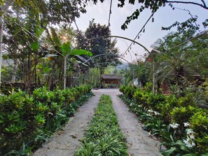 Un sendero en un jardín que lleva a una construcción con techo de paja a lo lejos.