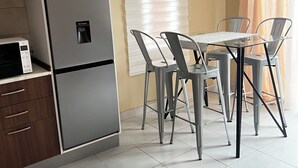 Een kleine keuken met een koelkast, een magnetron en een eethoek met een tafel en stoelen.