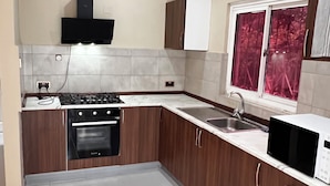 Een keuken met een gasfornuis, oven, magnetron en een raam met rode gordijnen.