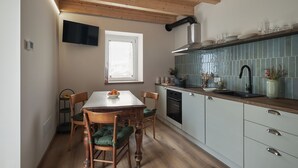 A kitchen with wooden cabinets, a tiled backsplash, a dining table with chairs, and a window. - Historic 1940s Watermill: A Designer Retreat in the Italian Alps (Cerete Basso)