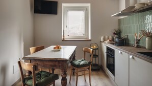 A compact kitchen with a dining table, chairs, a TV mounted on the wall, a window, and a stove. - Historic 1940s Watermill: A Designer Retreat in the Italian Alps (Cerete Basso)