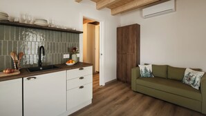 A kitchen with a wooden ceiling, a green tiled backsplash, a white cabinet, and a green sofa with a forest-themed pillow. - Historic 1940s Watermill: A Designer Retreat in the Italian Alps (Cerete Basso)