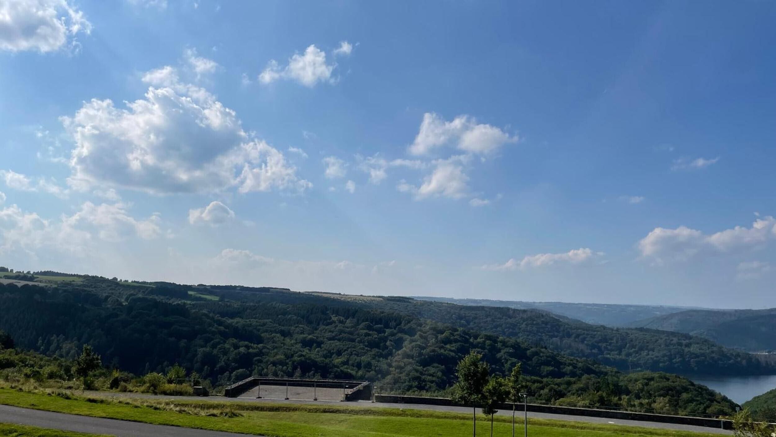 A view of a hilly landscape with a road, a building, and a body of water in the distance.