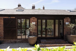 A brick building with large windows and a door, potted plants, and a clear sky.