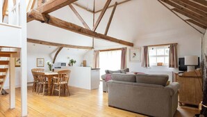 A spacious living area with wooden beams, a dining table with chairs, a grey sofa, and a television. - Wren Barn - Cosy 2-bed converted barn in Sidlesham (Sidlesham)