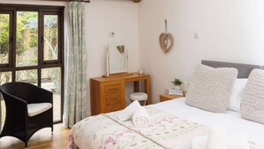 Ein Schlafzimmer mit Dachfenster, Holzbalken, einem Bett mit Blumenmuster, einem Nachttisch, einem Sessel und Blick durch ein Fenster.
