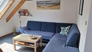 Una sala de estar moderna con un sofá azul, una mesa de centro de vidrio y un cuadro de una playa.