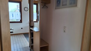 Un estrecho pasillo con una ventana, un reloj y una puerta que da a una habitación.
