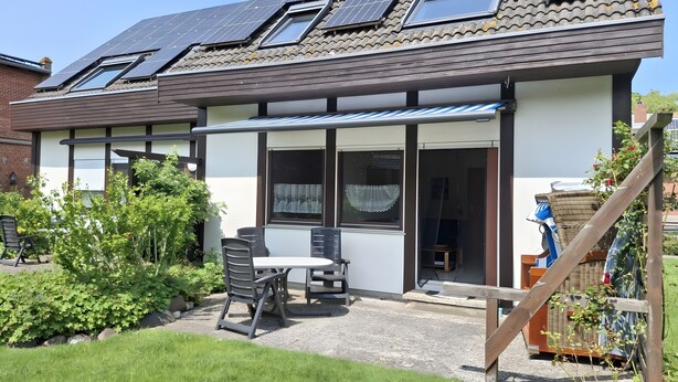 A residential building with solar panels, a covered patio with chairs, and a garden. - Holiday Apartment for 4 Guests (64 m²) on Fehmarn (Fehmarn)