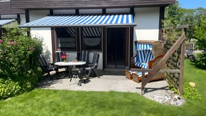 A patio with a table and chairs, a wicker chair, and a striped awning. - Holiday Apartment for 4 Guests (64 m²) on Fehmarn (Fehmarn)
