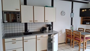 Een keuken met witte kastjes, een inbouwoven, een koffiezetapparaat, en een eethoek met een tafel en stoelen.