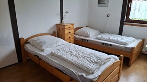 Two wooden bunk beds with white bedding, a wooden dresser with a lamp, and a window with a view of greenery. - Holiday Apartment for 1–5 Guests (64 m²) in Fehmarn (Fehmarn)