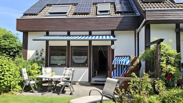Een huis met zonnepanelen, een overdekt terras met stoelen en een tuin.